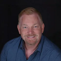 Portrait of William R. Mayer smiling against a dark background.