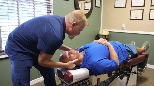 Chiropractor positioning a patient’s neck while the patient lies on a chiropractic table.